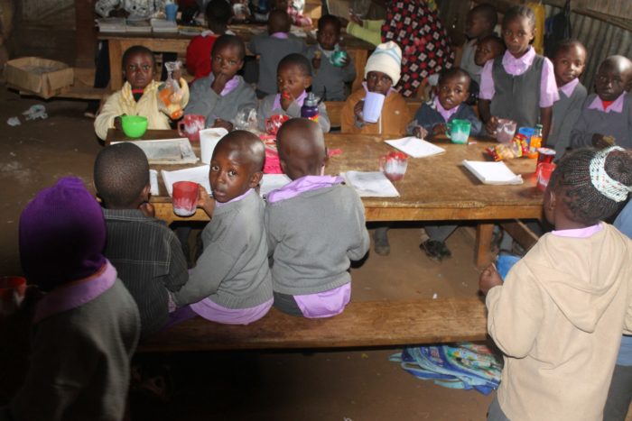 Schoolchildren sharing a meal around classroom tables.
