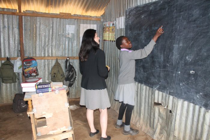 A teacher helping a student write on the classroom chalkboard.